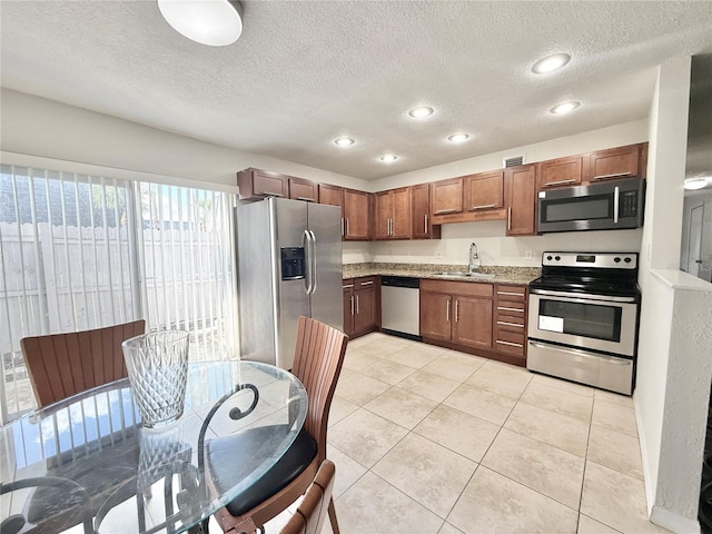 kitchen with appliances with stainless steel finishes, sink, light tile patterned floors, light stone counters, and a textured ceiling