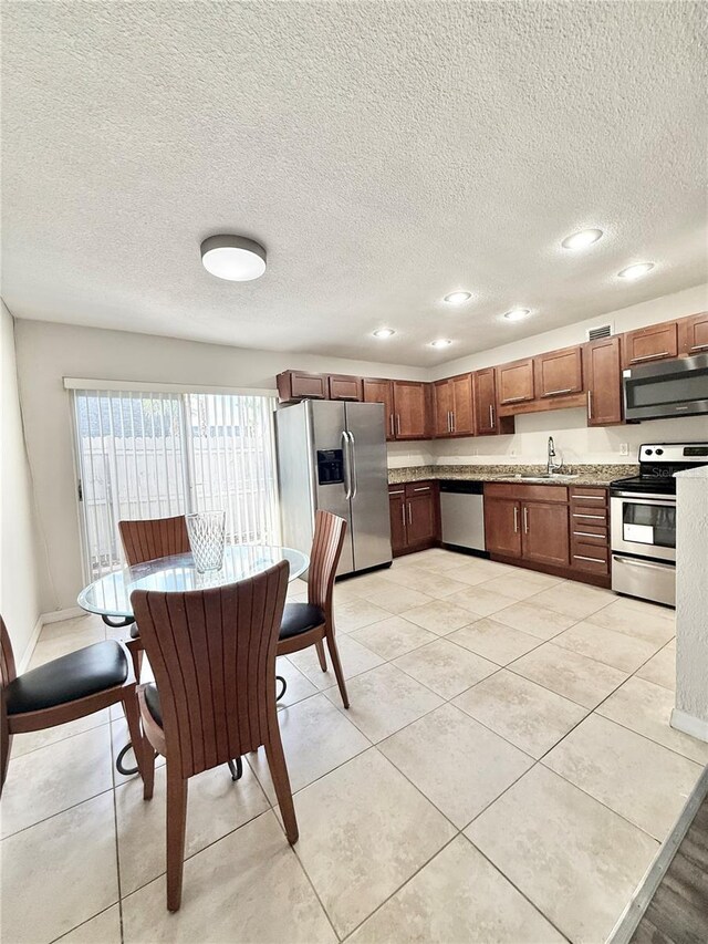 kitchen with stainless steel appliances, sink, light tile patterned floors, and a textured ceiling