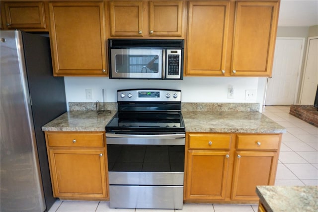 kitchen with light stone counters, light tile patterned flooring, and stainless steel appliances