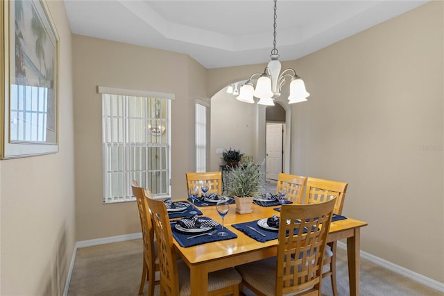 dining room with a raised ceiling, light carpet, and a notable chandelier