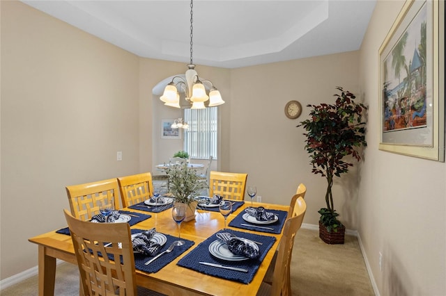 carpeted dining area featuring a chandelier and a tray ceiling