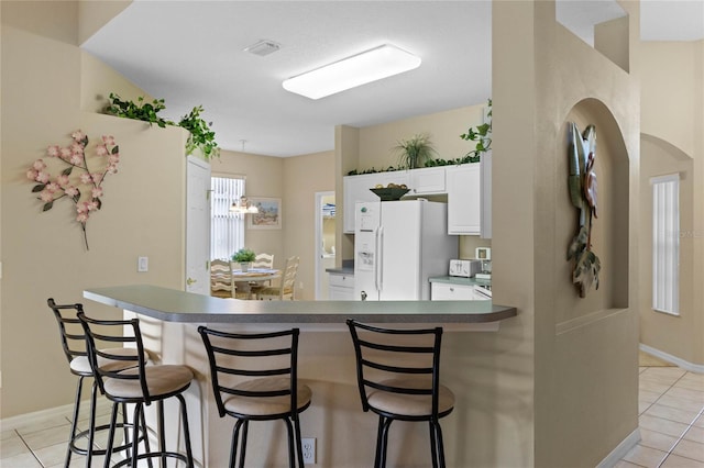 kitchen featuring a kitchen breakfast bar, white cabinetry, light tile patterned flooring, and white refrigerator with ice dispenser