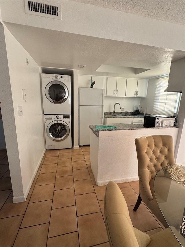 kitchen with white cabinetry, stacked washing maching and dryer, white refrigerator, a textured ceiling, and light tile patterned floors