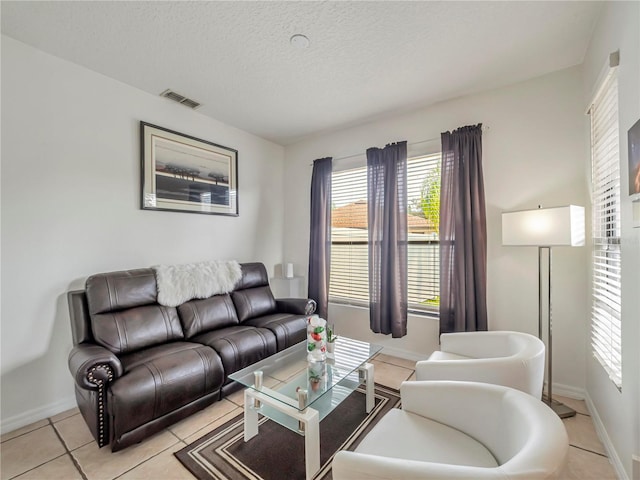 living room featuring light tile patterned floors, visible vents, a textured ceiling, and baseboards