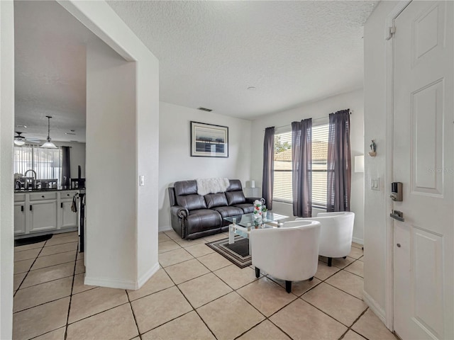 living room featuring light tile patterned floors, visible vents, baseboards, and a textured ceiling