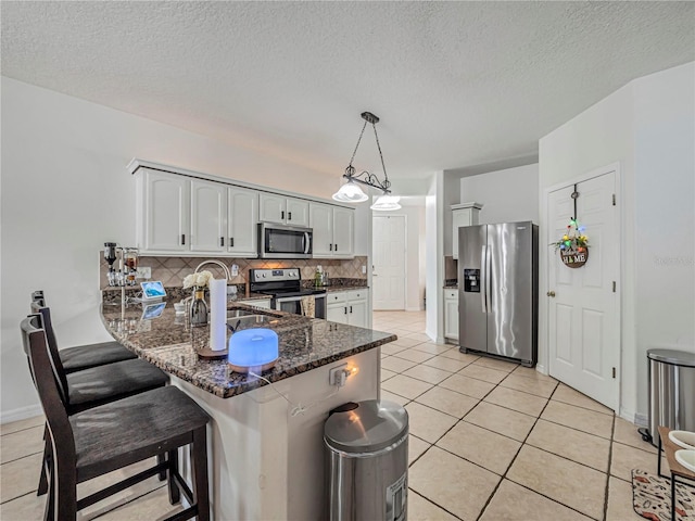 kitchen with stainless steel appliances, light tile patterned floors, pendant lighting, white cabinetry, and tasteful backsplash