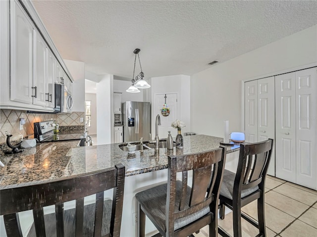 kitchen featuring light tile patterned floors, a peninsula, dark stone counters, stainless steel appliances, and decorative backsplash