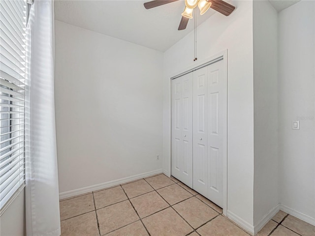 unfurnished bedroom featuring light tile patterned floors, a closet, baseboards, and a ceiling fan