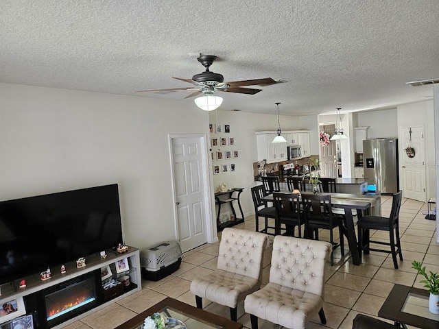 living room with visible vents, a textured ceiling, light tile patterned flooring, and a ceiling fan