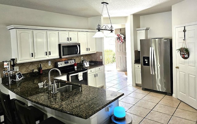 kitchen with kitchen peninsula, hanging light fixtures, white cabinetry, dark stone counters, and appliances with stainless steel finishes