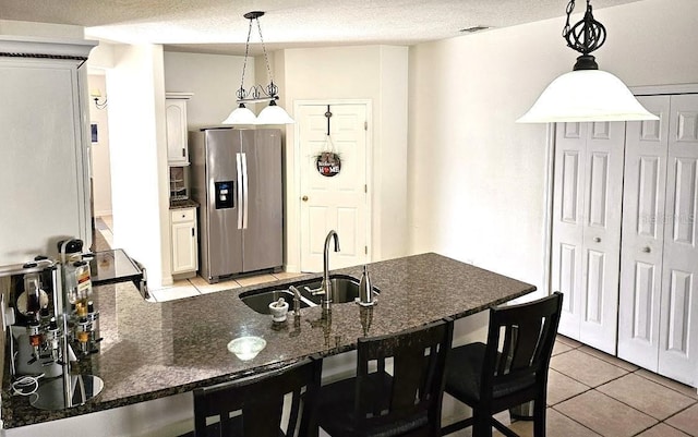 kitchen with light tile patterned floors, a peninsula, stainless steel fridge, a textured ceiling, and a sink