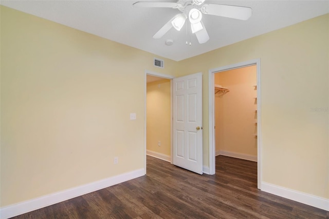 unfurnished bedroom with ceiling fan, a spacious closet, dark wood-type flooring, and a closet