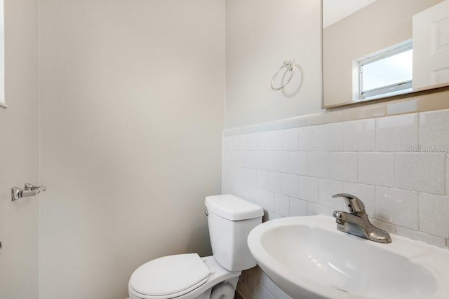 bathroom featuring toilet, tile walls, and sink