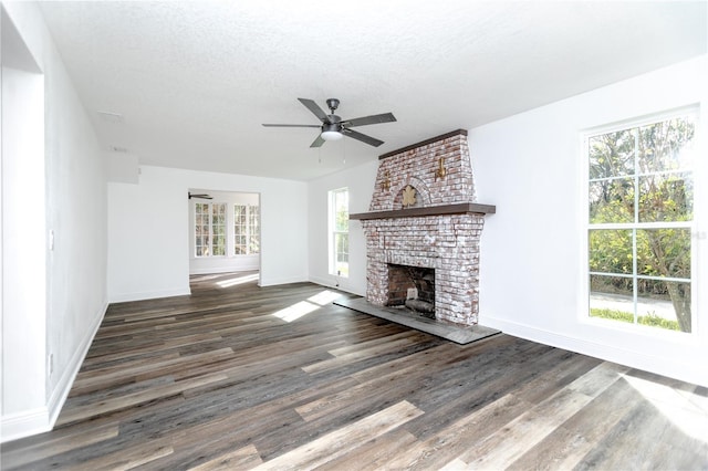 unfurnished living room featuring a textured ceiling, a brick fireplace, plenty of natural light, and dark wood-type flooring