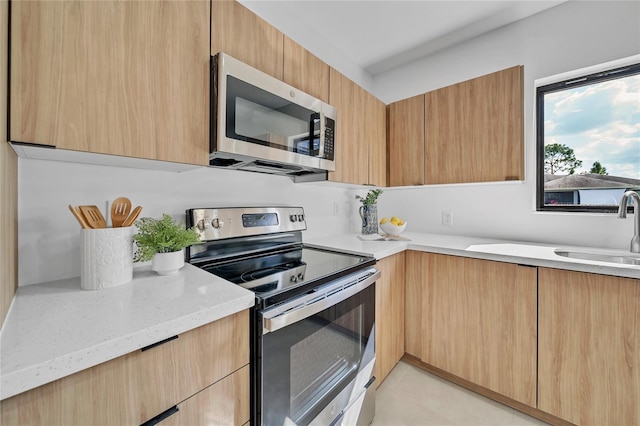 kitchen with light stone countertops, appliances with stainless steel finishes, light brown cabinets, and sink