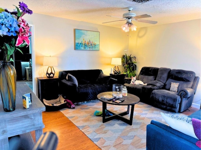 living room with wood-type flooring, ceiling fan, and a textured ceiling