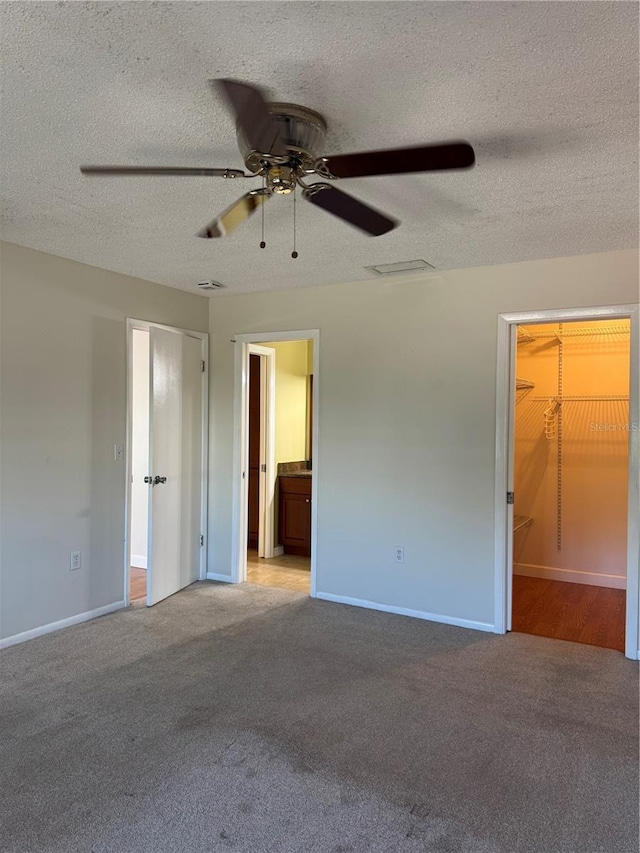 unfurnished bedroom with light colored carpet, a closet, ensuite bath, and a textured ceiling