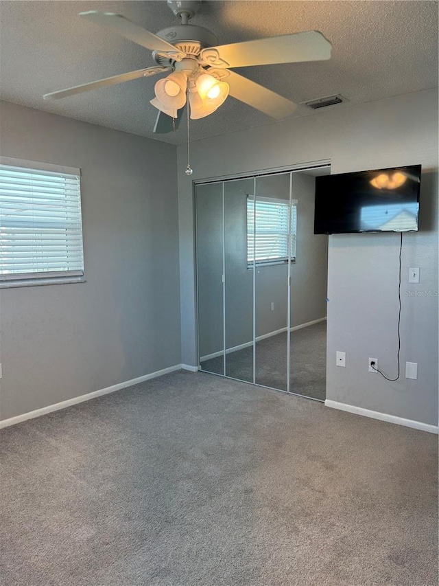 unfurnished bedroom with ceiling fan, carpet, a textured ceiling, and a closet