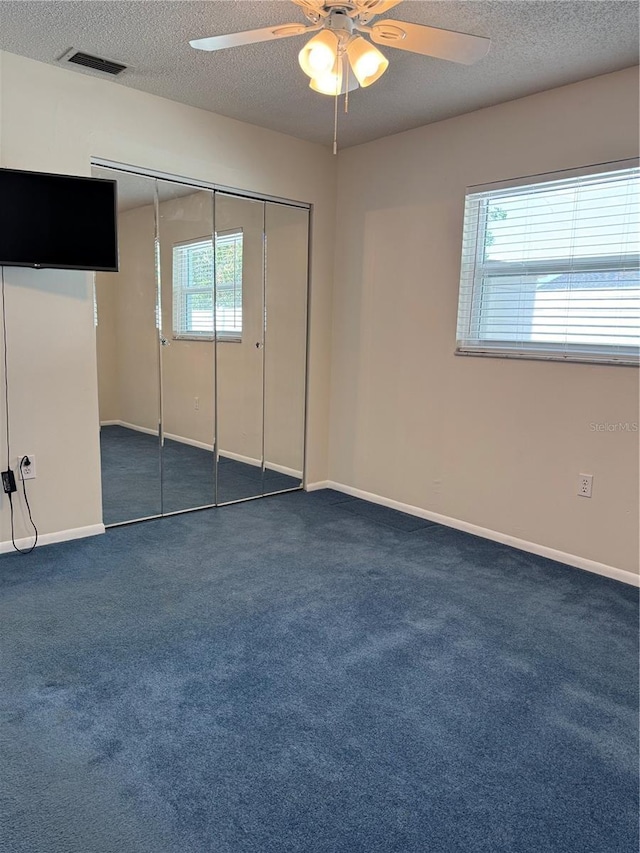 unfurnished bedroom with multiple windows, dark carpet, and a closet