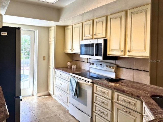 kitchen featuring appliances with stainless steel finishes, dark stone countertops, light tile patterned floors, and cream cabinetry