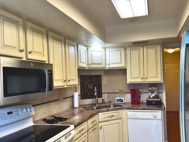 kitchen featuring sink, white appliances, backsplash, cream cabinets, and dark stone counters