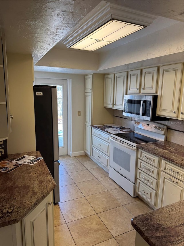 kitchen featuring dark stone countertops, appliances with stainless steel finishes, light tile patterned floors, and cream cabinets