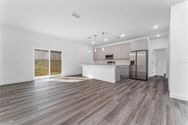 kitchen featuring hanging light fixtures, stainless steel appliances, light hardwood / wood-style floors, gray cabinets, and a kitchen island with sink