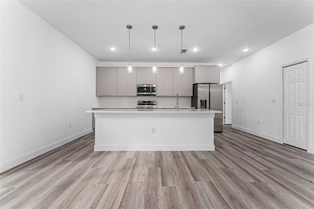 kitchen featuring stainless steel appliances, gray cabinets, a center island with sink, and sink