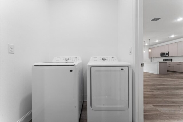 clothes washing area featuring wood-type flooring, sink, and washing machine and clothes dryer