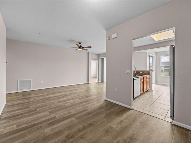 unfurnished living room featuring ceiling fan, light hardwood / wood-style floors, sink, and a skylight