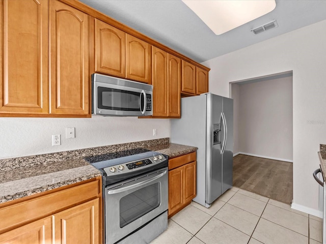 kitchen featuring dark stone countertops, light tile patterned floors, and stainless steel appliances