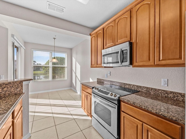 kitchen with decorative light fixtures, stainless steel appliances, dark stone counters, and light tile patterned flooring