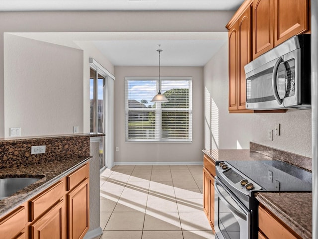 kitchen with appliances with stainless steel finishes, decorative light fixtures, light tile patterned floors, and dark stone countertops