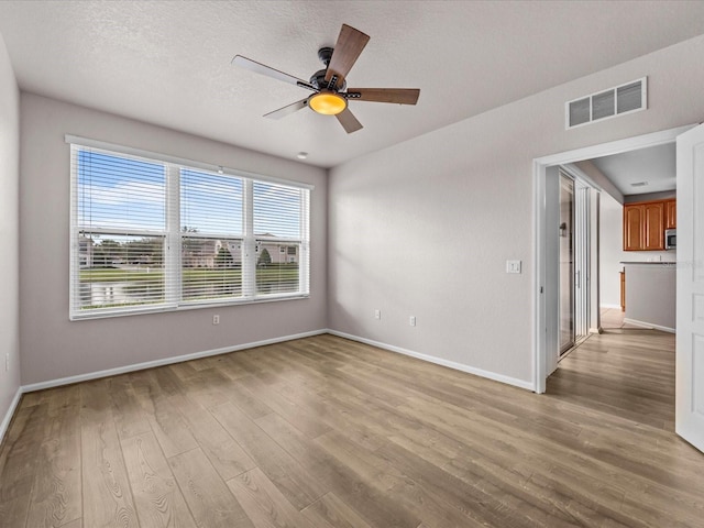 empty room with ceiling fan, light hardwood / wood-style flooring, and a textured ceiling