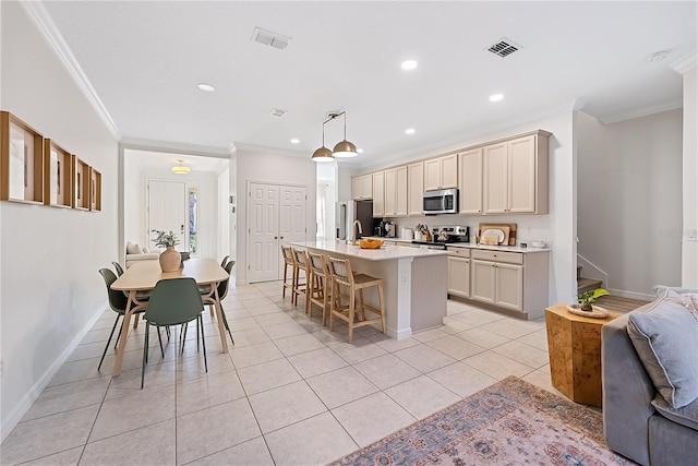 kitchen featuring hanging light fixtures, a breakfast bar area, a kitchen island with sink, appliances with stainless steel finishes, and ornamental molding