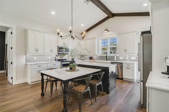 kitchen with vaulted ceiling with beams, white cabinetry, pendant lighting, and stainless steel appliances