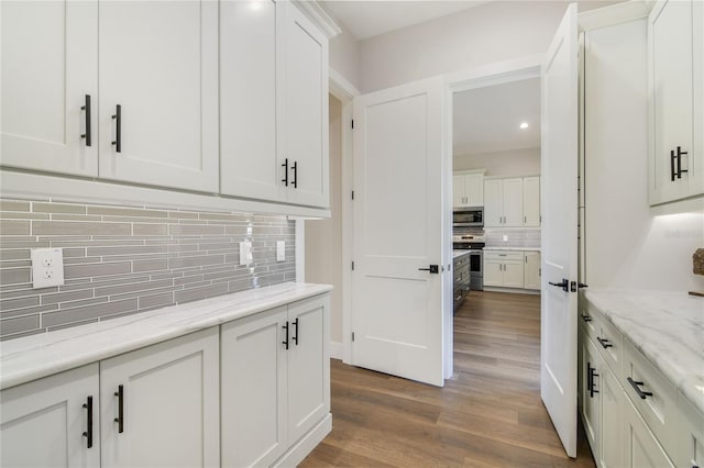 kitchen with white cabinetry, stainless steel appliances, light stone counters, decorative backsplash, and light wood-type flooring