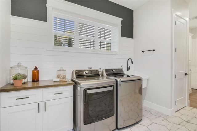 laundry area featuring wood walls, cabinets, separate washer and dryer, and sink