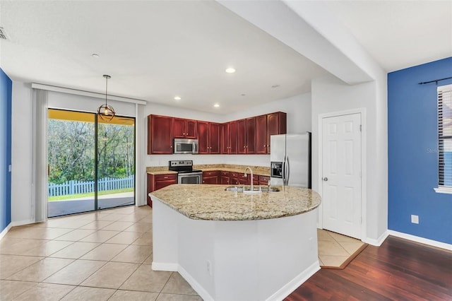 kitchen with sink, light tile patterned floors, pendant lighting, a kitchen island with sink, and appliances with stainless steel finishes