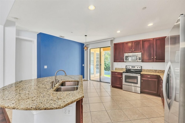 kitchen featuring light stone countertops, pendant lighting, stainless steel appliances, a center island with sink, and sink