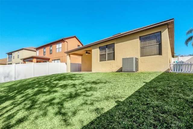 rear view of property featuring central air condition unit, a yard, and ceiling fan