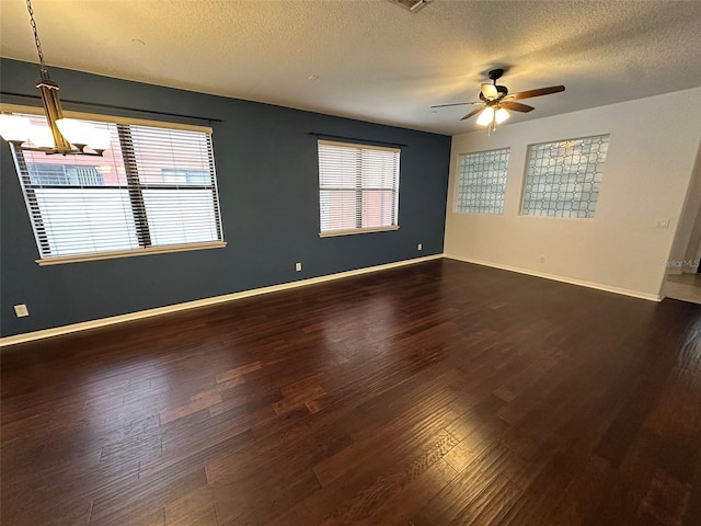 unfurnished room with ceiling fan with notable chandelier, a textured ceiling, a healthy amount of sunlight, and dark hardwood / wood-style floors