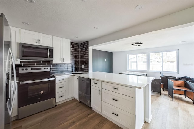 kitchen featuring hardwood / wood-style floors, white cabinetry, kitchen peninsula, and appliances with stainless steel finishes