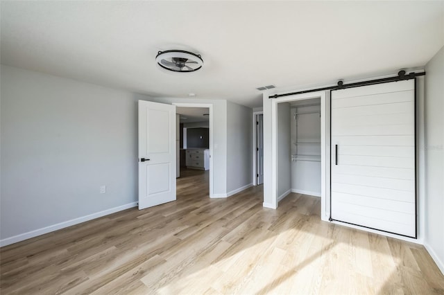 unfurnished bedroom with a barn door, a closet, and light hardwood / wood-style floors