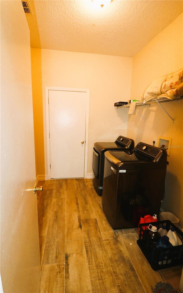 clothes washing area with hardwood / wood-style flooring, separate washer and dryer, and a textured ceiling