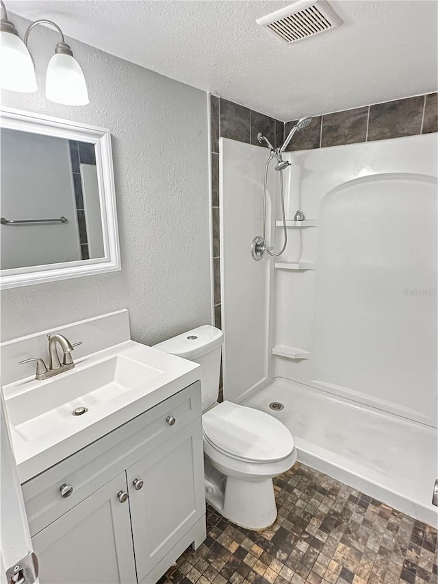 bathroom with vanity, toilet, tiled shower, and a textured ceiling