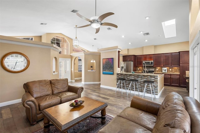 living room featuring ceiling fan, vaulted ceiling with skylight, and hardwood / wood-style flooring