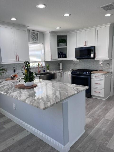 kitchen with black appliances, white cabinets, light stone countertops, and sink