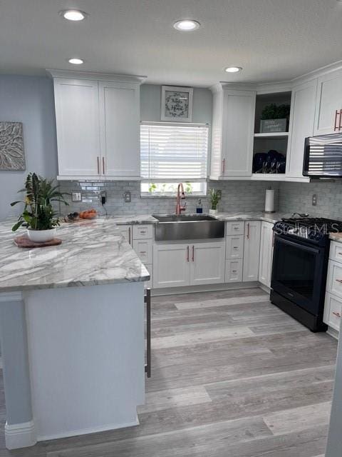 kitchen with black gas range, light wood finished floors, white cabinets, open shelves, and a sink