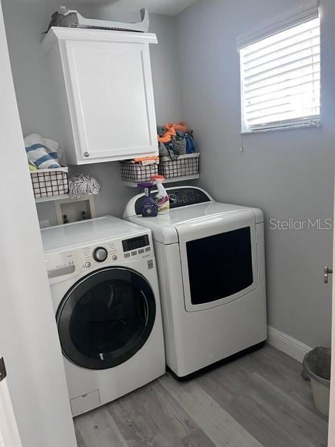 clothes washing area featuring separate washer and dryer, cabinets, and light hardwood / wood-style floors